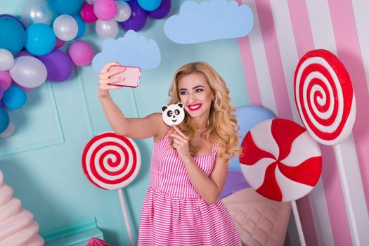 Portrait of amazing sweet-tooth woman in pink dress holding candies and posing on background decorated with huge ice cream. Lollipop panda