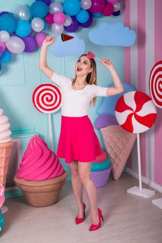Portrait of amazing sweet-tooth woman in pink dress holding candies and posing on background decorated with huge ice cream. Lollipop watermelon
