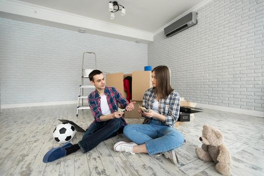 Young couple counting money while sitting on floor in new apartment