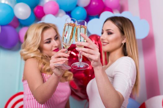 Two young women in pink dresses hold glasses of champagne.