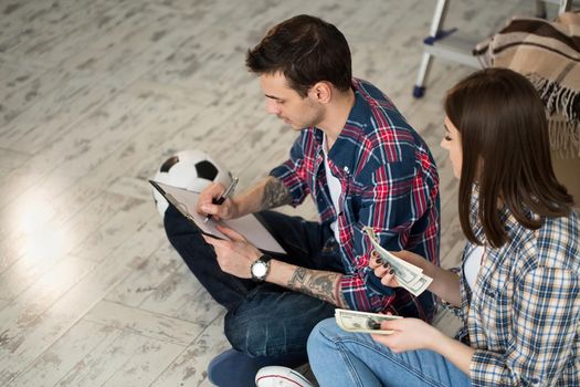 Young couple counting money while sitting on floor in new apartment