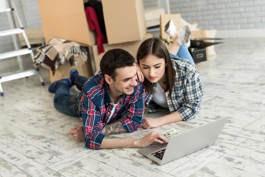 Portrait of a cute young couple lying on the floor at home and managing budget using laptop