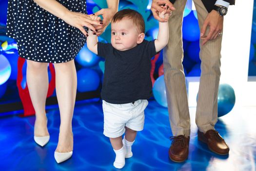 Little boy holds the hand of his mother and father and tries to take the first steps.