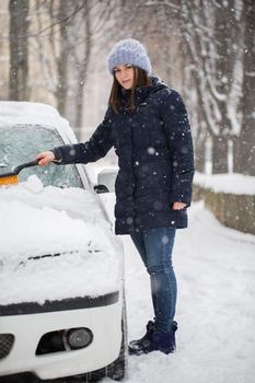 A woman removes snow from the windshield of a car
