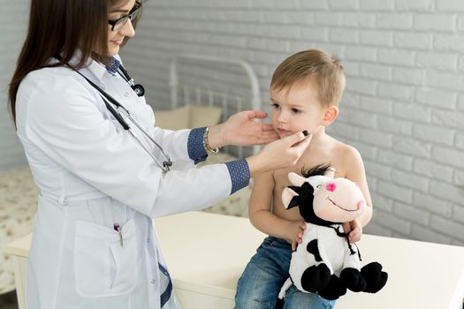 Pediatrician examining thyroid gland of little boy in clinic