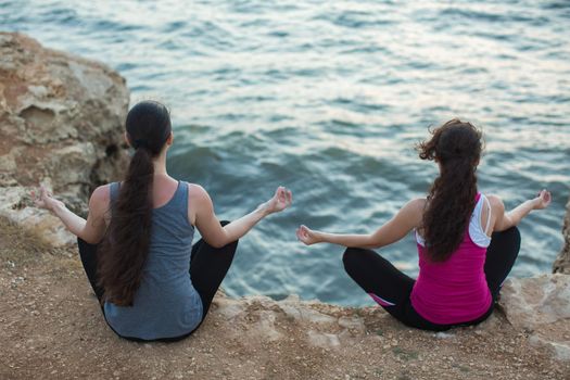 A couple of girls practicing yoga on the beach at sunset.