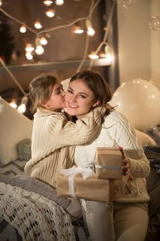 Beautiful mother and daughter opening a magical Christmas gift in the cozy interior of the house. New year