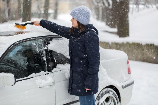 Woman cleaning snow from the car in the winter