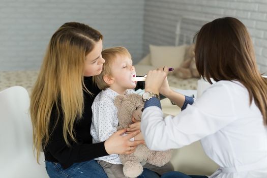 Doctor examine child's throat. Boy and mother at pediatrician office.