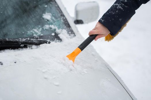 Woman cleaning snow from the car in the winter