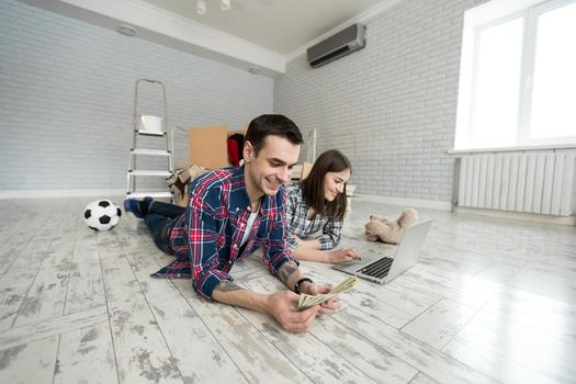 Portrait of a cute young couple lying on the floor at home and managing budget using laptop