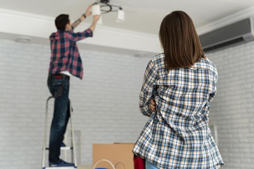 Young couple moving in new house, changing a light bulb.