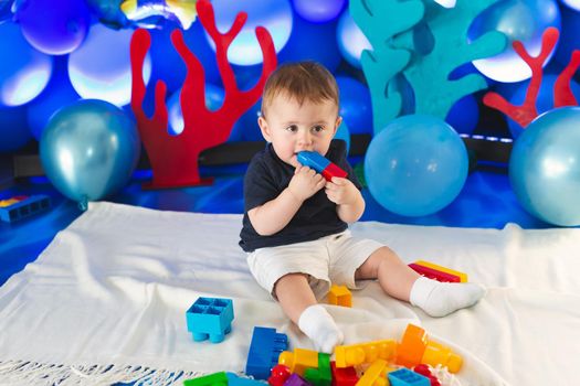 Small boy in a smart suit sits on the floor and plays with a construction kit.