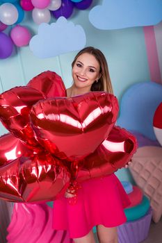 Fashion portrait of young woman in pink dress with an air balloons, candy on a colorful background.