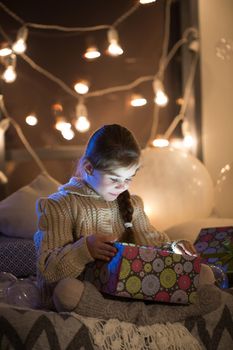 Beautiful little girl opens a magical Christmas gift in the cozy interior of the house. New year