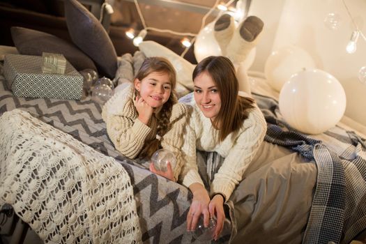 Beautiful mother and daughter lying on the bed on Christmas eve in the cozy interior of the house. New year