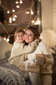 Beautiful mother and daughter opening a magical Christmas gift in the cozy interior of the house. New year