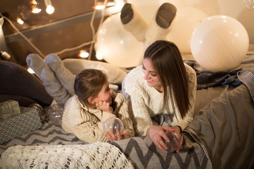 Beautiful mother and daughter lying on the bed on Christmas eve in the cozy interior of the house. New year