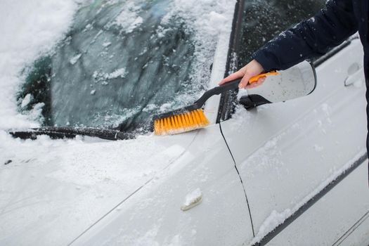 A woman removes snow from the windshield of a car