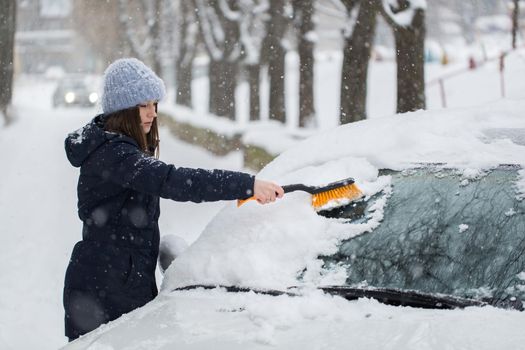 A woman removes snow from the windshield of a car