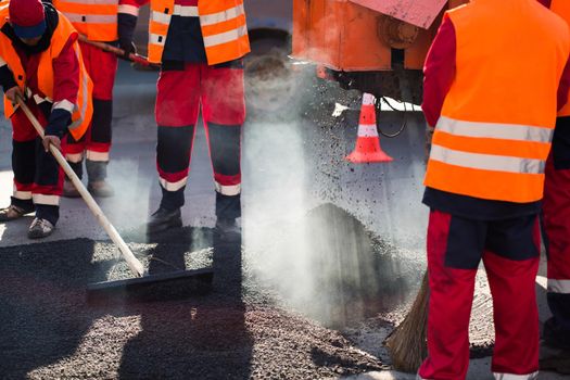 Worker leveling fresh asphalt on a road construction site, industrial buildings and teamwork