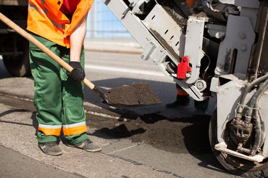 Road workers repair work. work sleeps shovel the material into the machine.