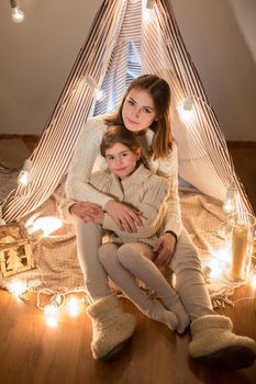 Beautiful mother and daughter, Christmas eve, sitting in the cosy interior. New year