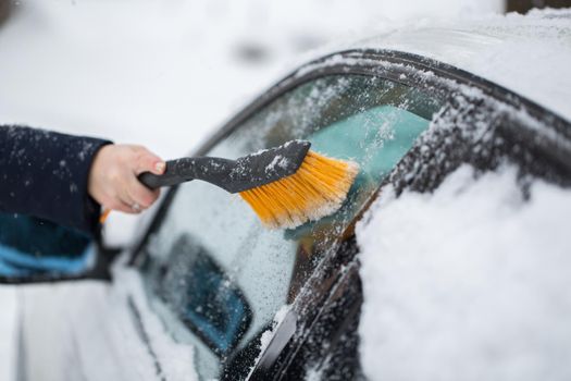 Woman cleaning snow from the car in the winter