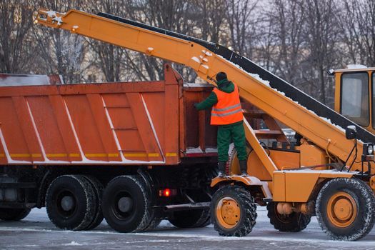 Tractor cleaning the road from the snow. Excavator cleans the streets of large amounts of snow in city. Workers sweep snow from road in winter, Cleaning road from snow storm.