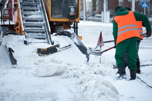 Tractor cleaning the road from the snow. Excavator cleans the streets of large amounts of snow in city. Workers sweep snow from road in winter, Cleaning road from snow storm.