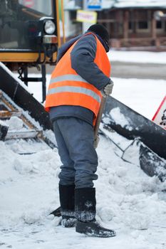 Tractor cleaning the road from the snow. Excavator cleans the streets of large amounts of snow in city. Workers sweep snow from road in winter, Cleaning road from snow storm.