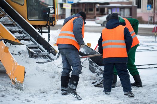 Tractor cleaning the road from the snow. Excavator cleans the streets of large amounts of snow in city. Workers sweep snow from road in winter, Cleaning road from snow storm.