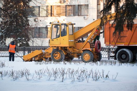 Tractor cleaning the road from the snow. Excavator cleans the streets of large amounts of snow in city. Workers sweep snow from road in winter, Cleaning road from snow storm.