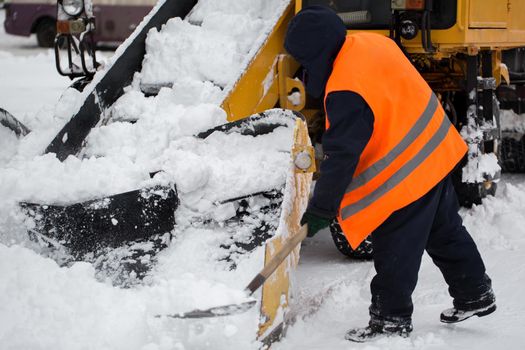 Claw loader vehicle removes snow from the road. Employees of municipal services helps shovel snow into a snowplow.