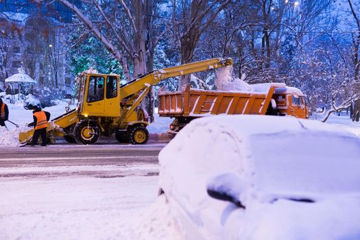 Claw loader vehicle removes snow from the road. A snowplow pours snow into a truck.