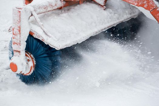 City service cleaning snow , a small tractor with a rotating brush clears a road in the city park from the fresh fallen snow on winter day