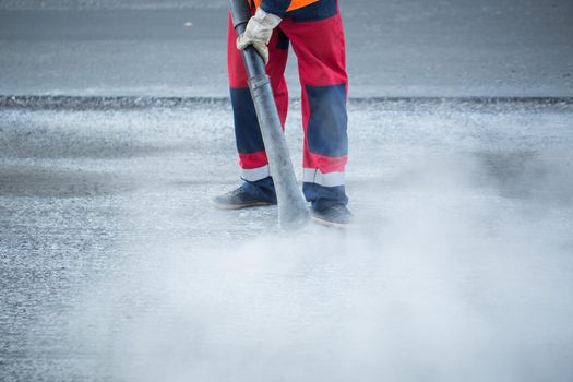 Worker with leaf-blower, cleaning out the dust for better asphalt adhesion, during tram track renewal works