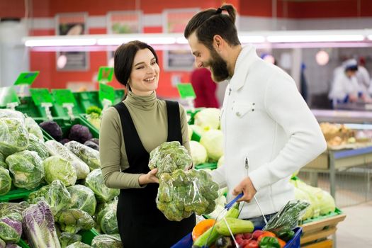 Portrait of a healthy couple looking at fruits and vegetables in the supermarket while shopping. Beautiful couple chooses cabbage in a supermarket