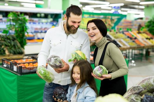 A young family with a daughter chooses vegetables in the supermarket.