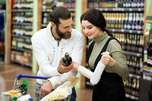 A young family, a man and a woman choose alcohol in a large supermarket.