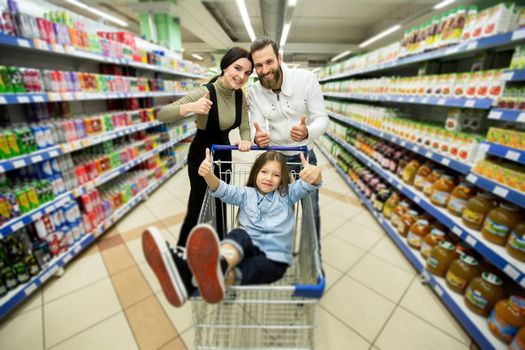 Beautiful young parents and their cute little daughter are smiling while choosing food in the supermarket.