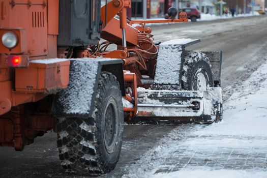 Tractor cleaning the road from the snow. Excavator cleans the streets of large amounts of snow in city. Workers sweep snow from road in winter, Cleaning road from snow storm.