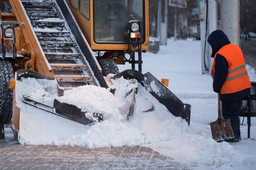 Tractor cleaning the road from the snow. Excavator cleans the streets of large amounts of snow in city. Workers sweep snow from road in winter, Cleaning road from snow storm.