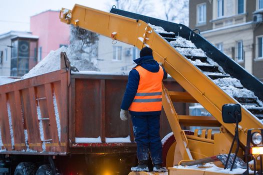 Snow cleaning tractor snow-removal machine loading pile of snow on a dump truck. Isolate. Snow plow outdoors cleaning street city after blizzard or snowfall.