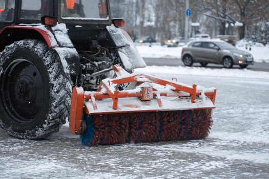 Tractor brushes snow on the road in the evening.