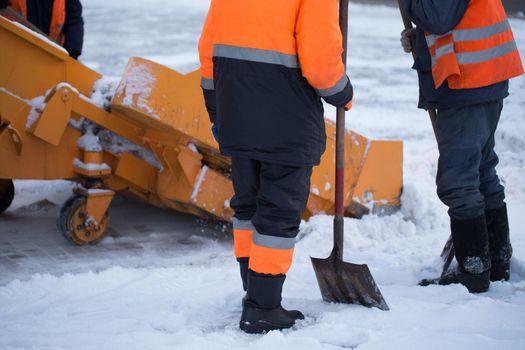 Tractor cleaning the road from the snow. Excavator cleans the streets of large amounts of snow in city. Workers sweep snow from road in winter, Cleaning road from snow storm.