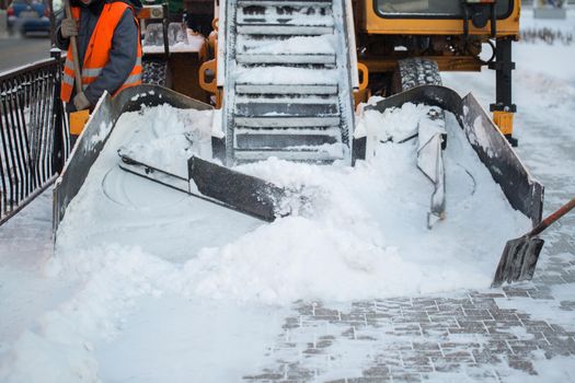 Tractor cleaning the road from the snow. Excavator cleans the streets of large amounts of snow in city. Workers sweep snow from road in winter, Cleaning road from snow storm.