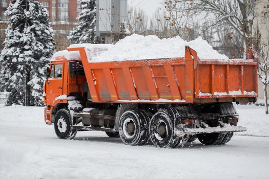 Dump truck full of snow driving through city street, snow hauling. Dump truck transports snow to dump site.