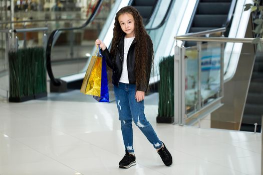 The happy child with color packages on the escalator, in shop of shopping center
