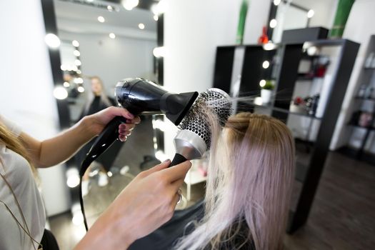 Drying long blonde hair with hair dryer and round brush